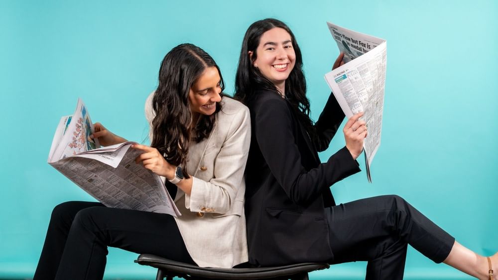 Two women sitting back-to-back reading newspapers at Novotel Sydney Olympic Park