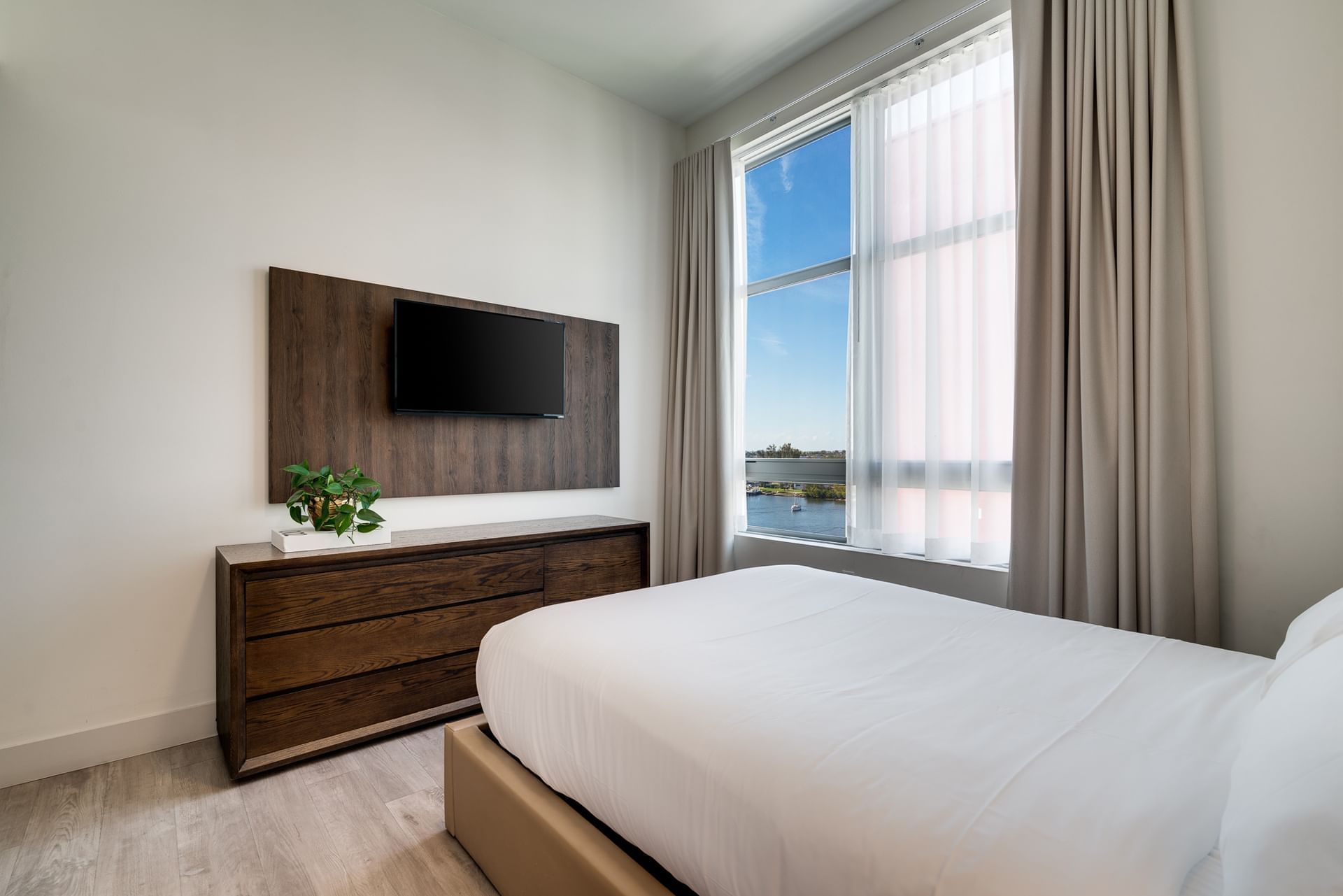 A hotel room with a bed, dresser, TV, and window