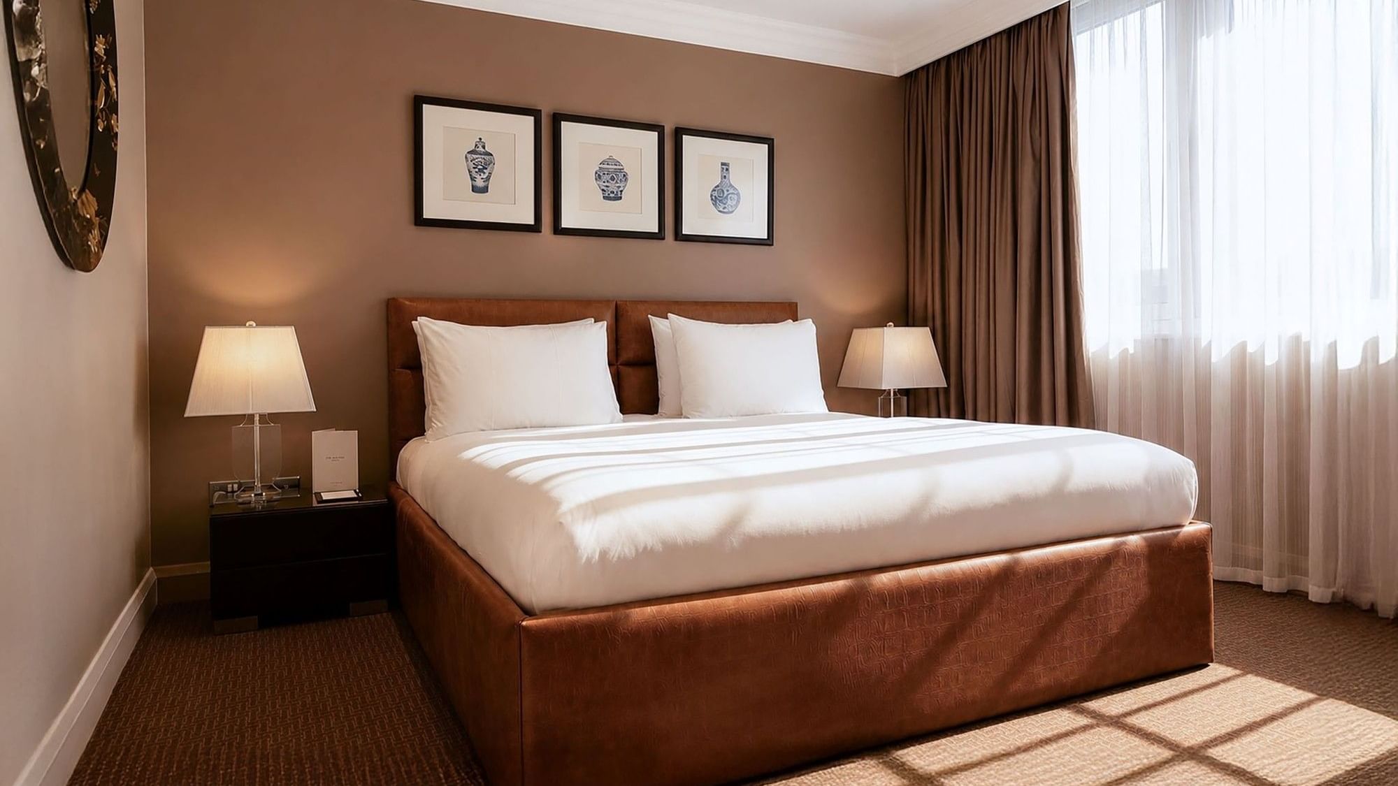 The Saffron Suite with brown upholstered bed, white linens, framed artwork, and sheer curtains at The May Fair Hotel, London.
