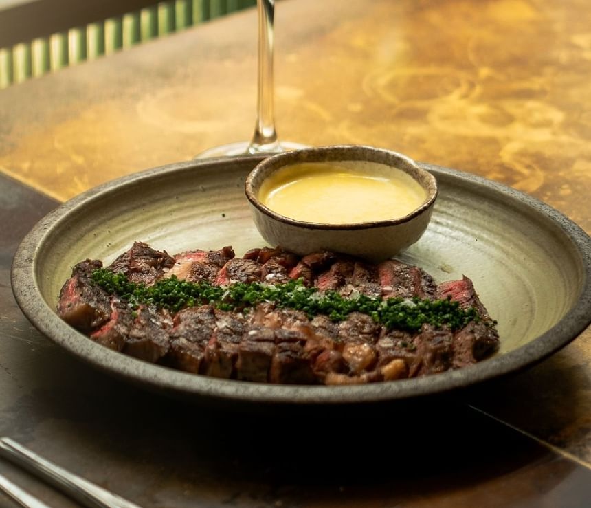 Red wine poured into a glass by a bowl of grilled steak and sauce served on a table at The Kitchens