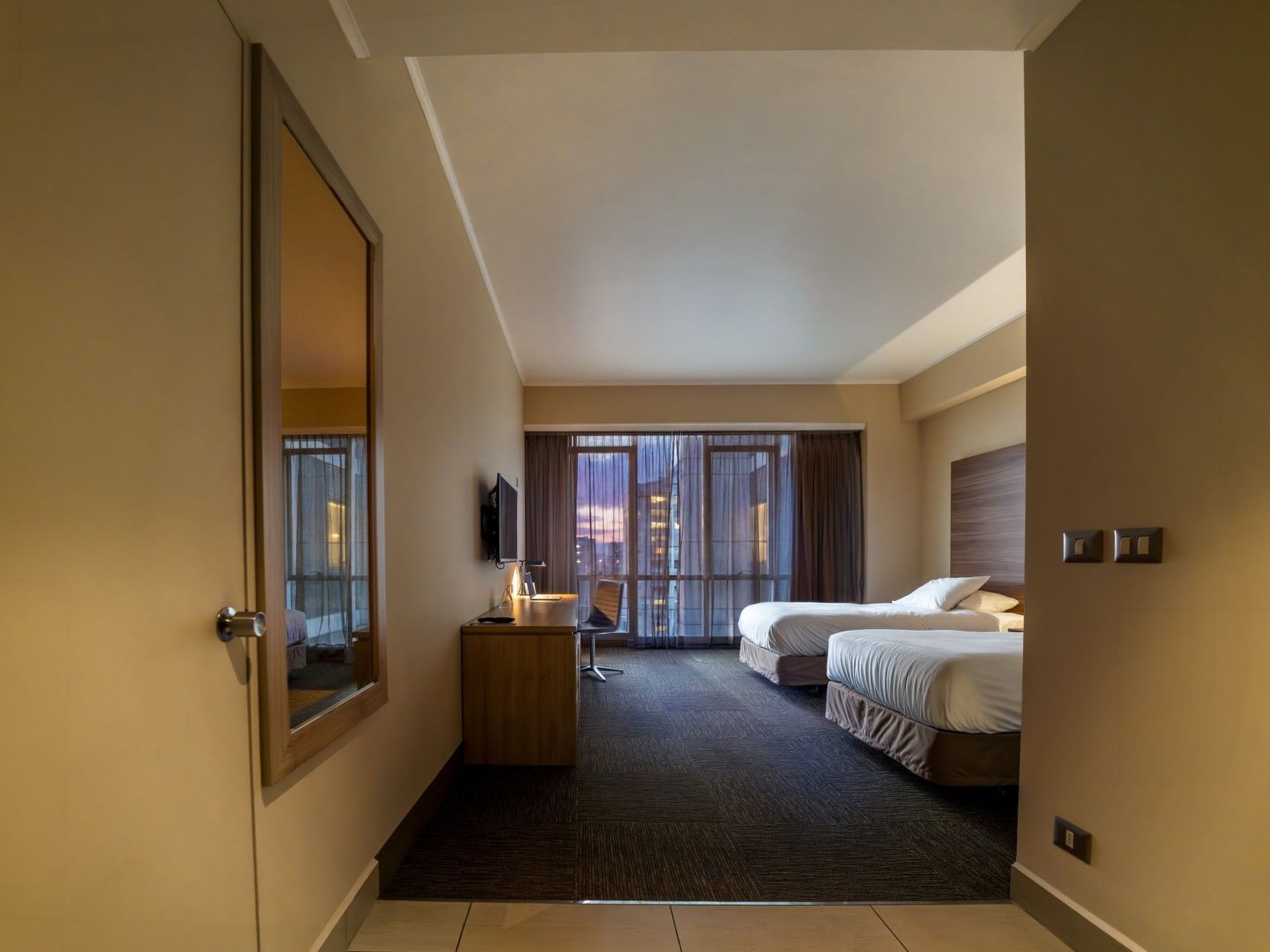 Interior de una habitación de hotel limpio y moderno, con dos camas y un escritorio, en el hotel HCC Costanera Concepción.