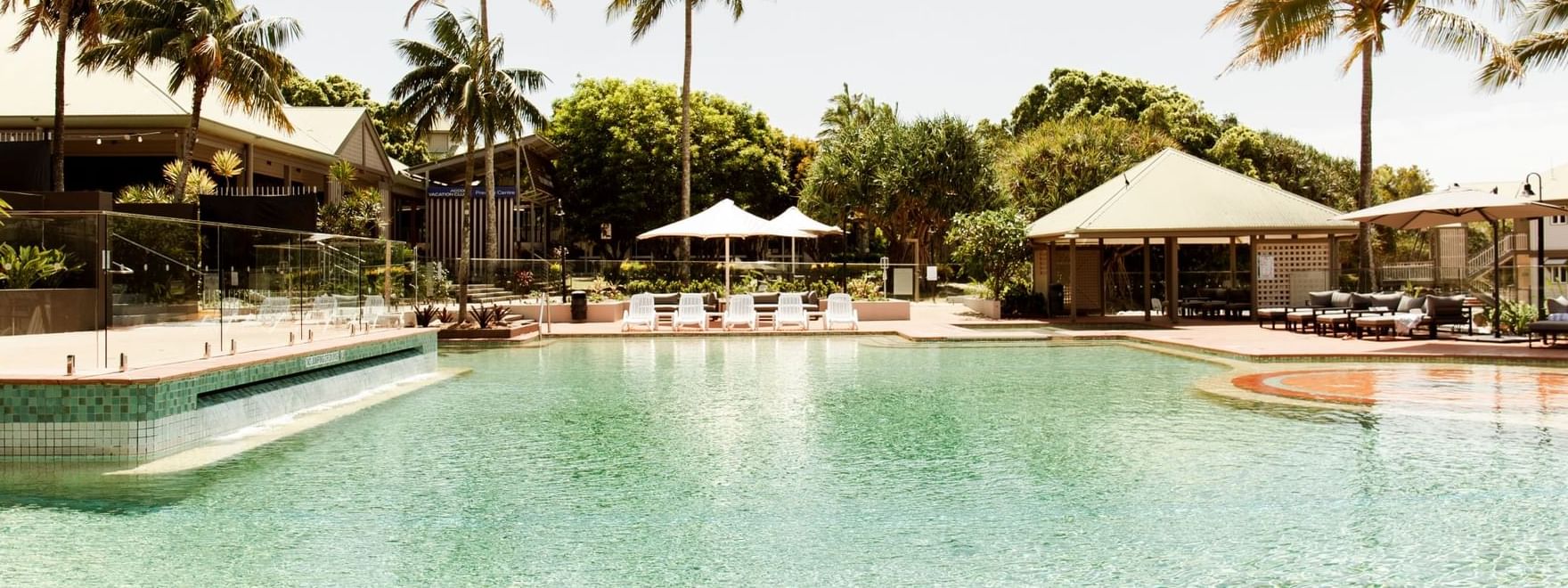 Lounge chairs and shaded cabanas by the pool, surrounded by palm trees at Novotel Sunshine Coast Resort