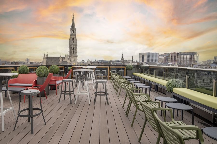 Dakterras met kleurrijke zitplaatsen en panoramisch uitzicht op de Brusselse skyline bij zonsondergang.