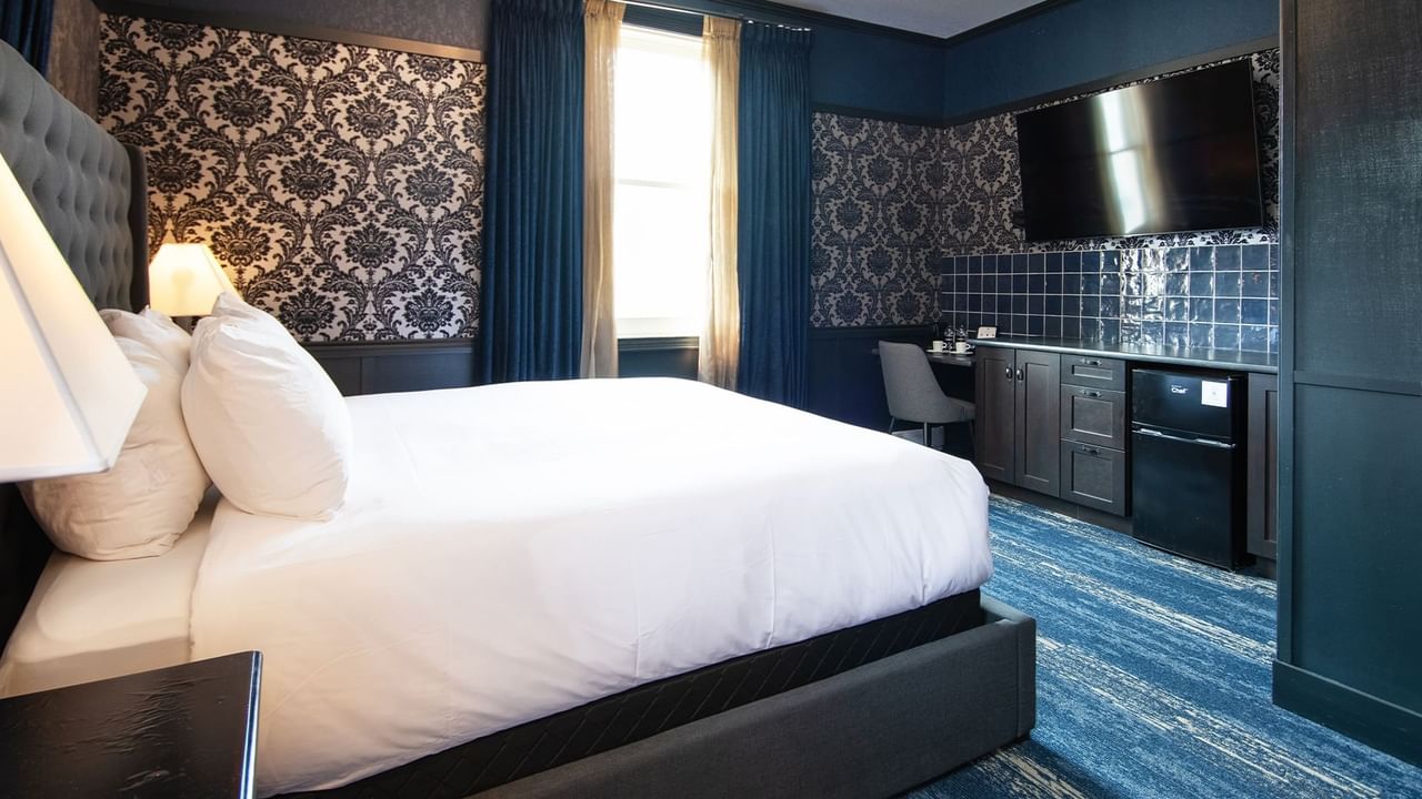 Hotel room with king bed, flat-screen TV, mini fridge, desk, chair, and window