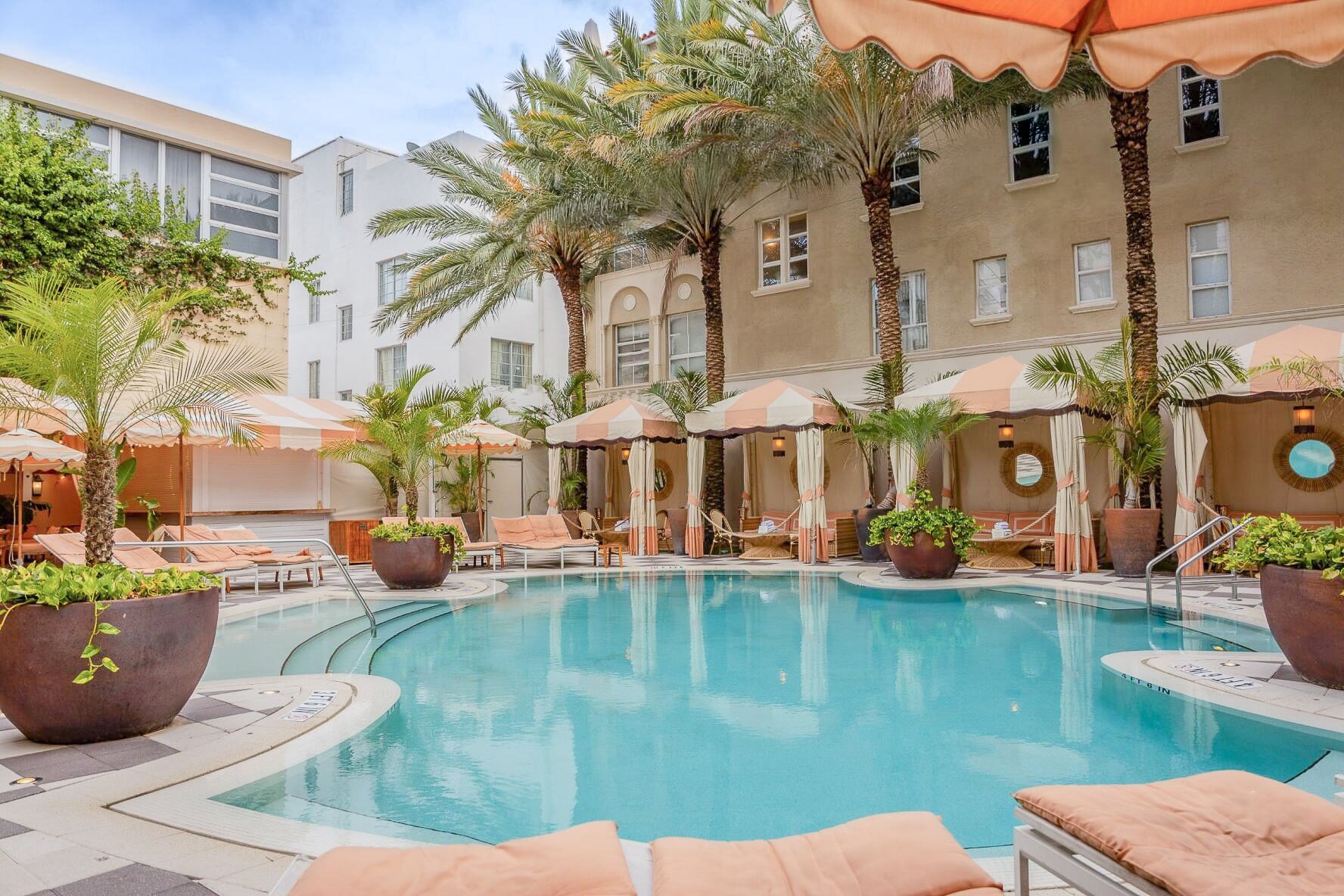 A swimming pool with a beige and white color scheme, lounge chairs, palms, and a canopied cabana area.