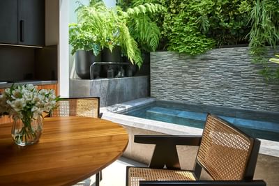 Chic dining area with a round table and a view of a small jacuzzi and lush green plants at Singular Signature Residences