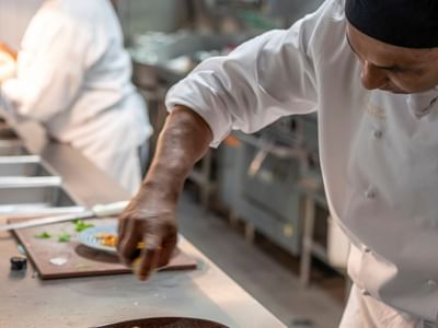 Chef seasoning a dish on a kitchen counter in Croft Restaurant at Amora Herencia Riverwalk Melbourne