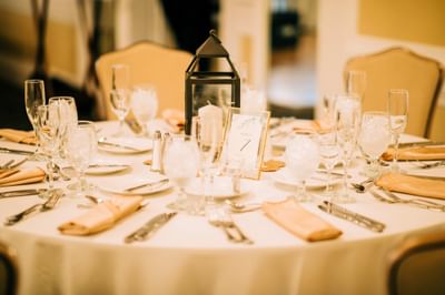 Elegant round dining table set with white linens near a central candle lantern at event hall in Avon Old Farms Hotel