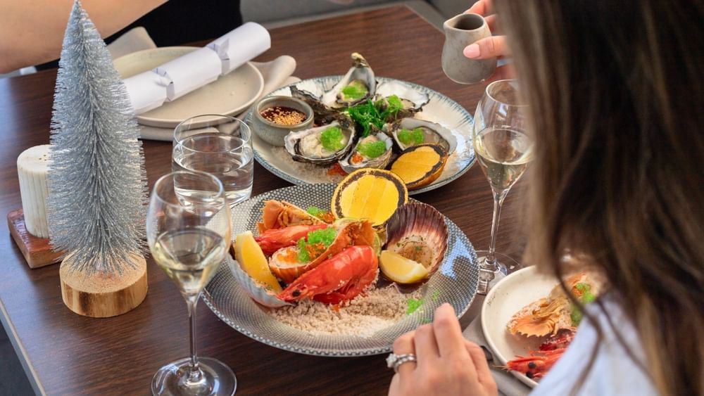 Festive seafood platter with oysters, lobster, and scallops served with white wine and a miniature Christmas tree.