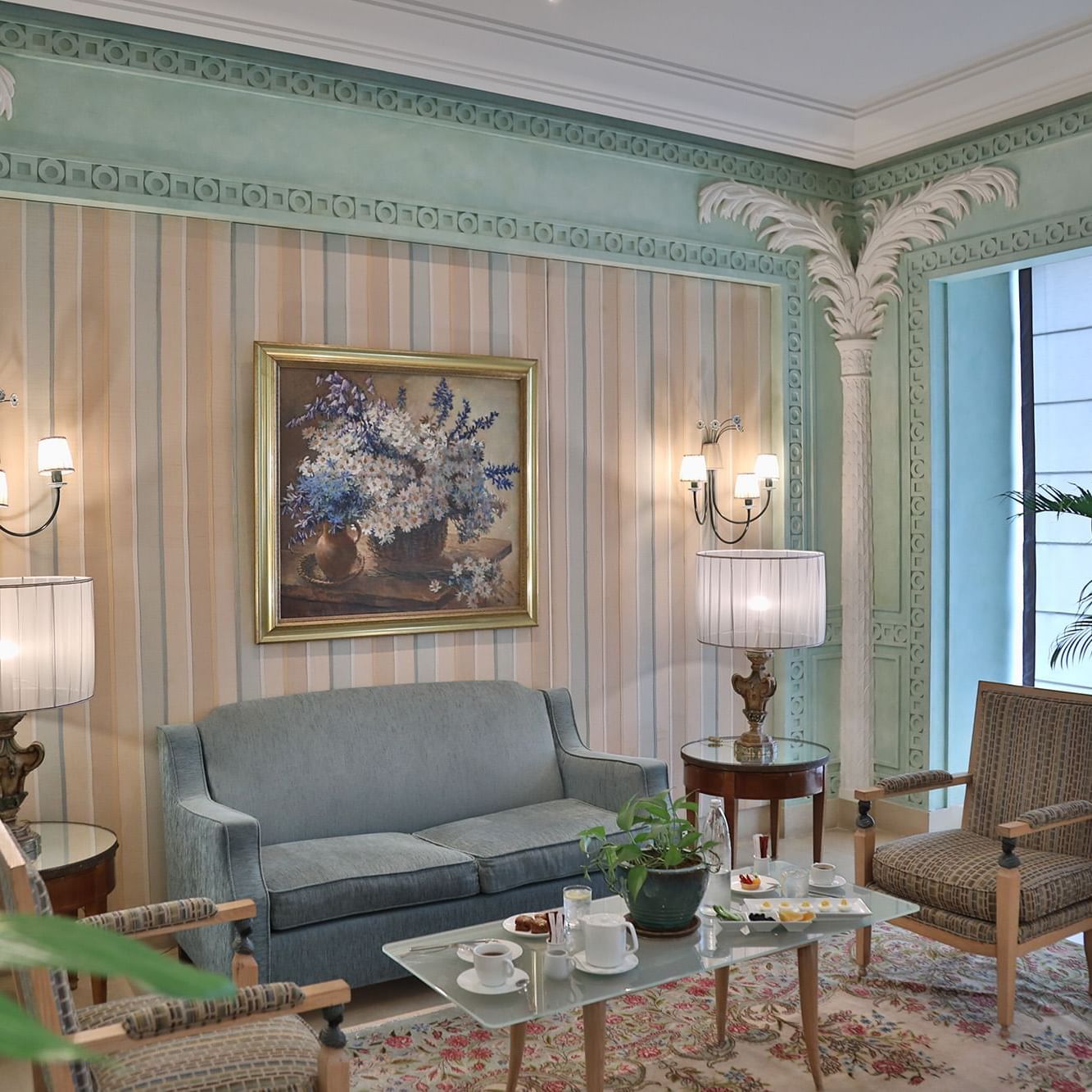 Un canapé bleu près de tables rondes en verre, sous des lampes et un tableau représentant des fleurs, dans le hall de l'hôtel Warwick Palm Beach