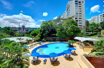 Vista aérea del área de la piscina al aire libre y tumbonas con el exterior del Hotel Dann Carlton Medellín 
