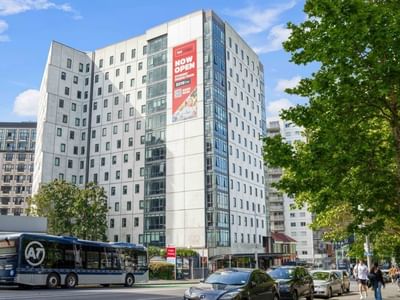 Modern UniLodge Wellesley Apartments building with traffic and pedestrians nearby.