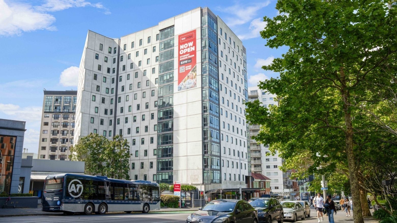 Modern UniLodge Wellesley Apartments building with traffic and pedestrians nearby.