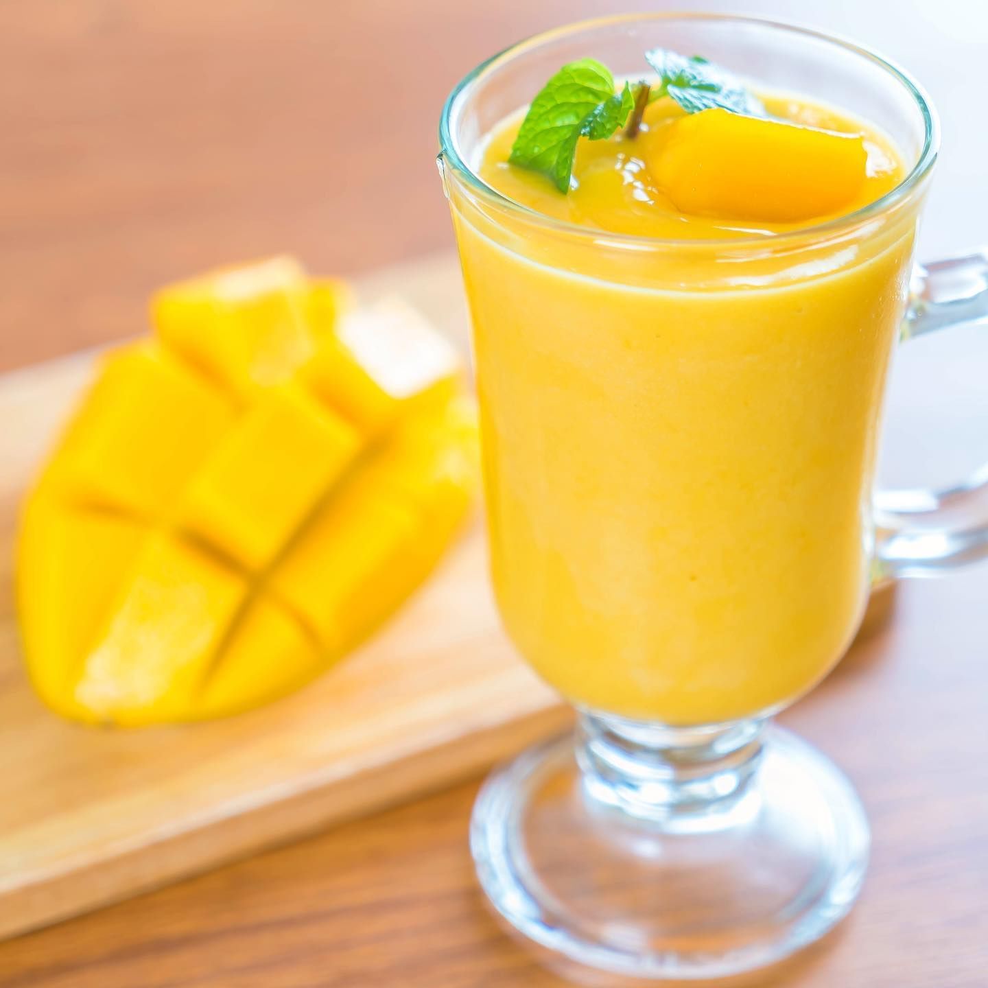 a glass of yellow smoothie with mango and mint on top