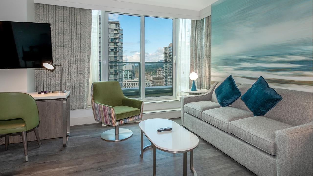 Hotel room with couch, chairs, desk, and large window.