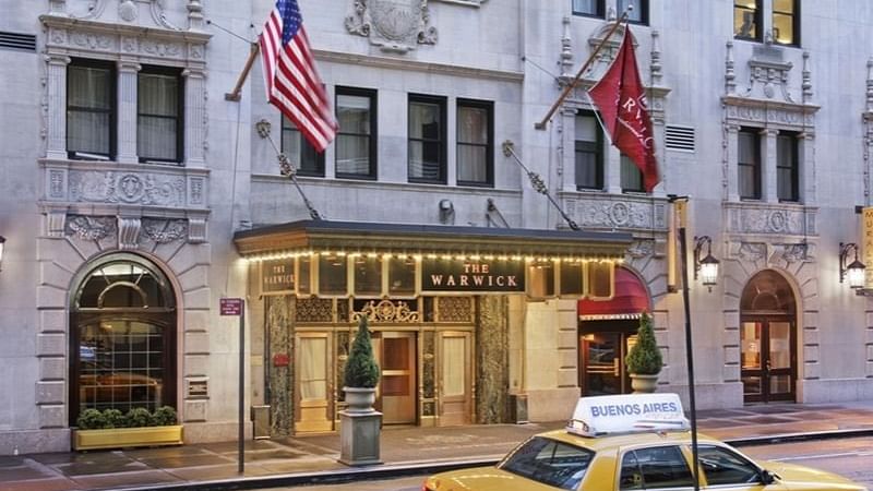 Classic yellow NYC taxi is parked on the street in front of The Warwick Hotel facade