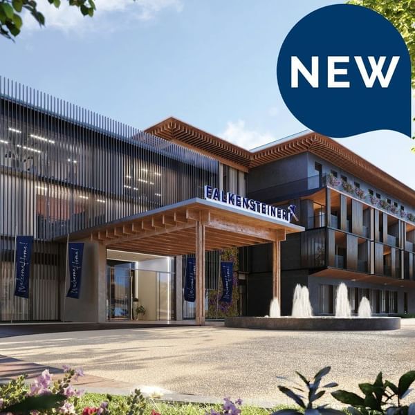 New Falkensteiner Hotel entrance with banners, wooden canopy, glass doors, and circular fountain.