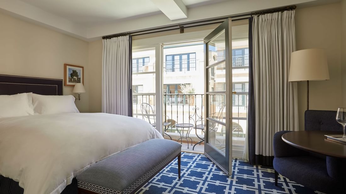 Sitting area and ottoman by the cozy bed in Deluxe King Suite with carpeted flooring at El Prado Hotel