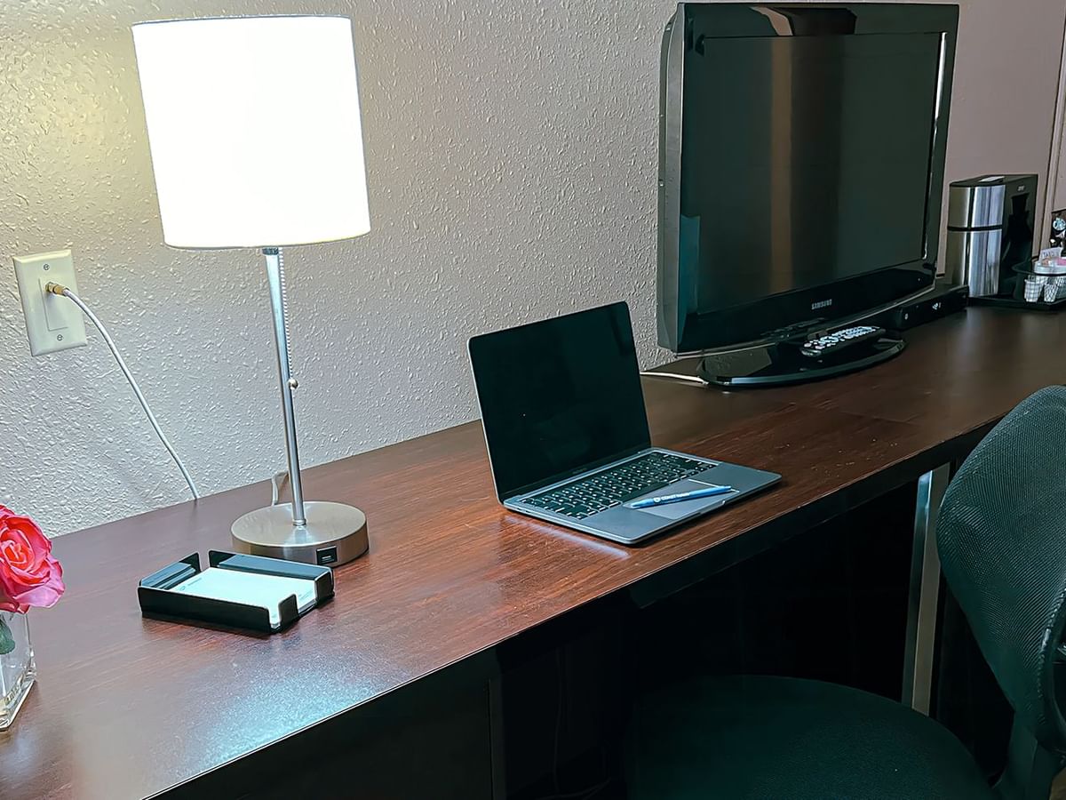 Table with computer, lamp, TV, coffee and tea, and flowers