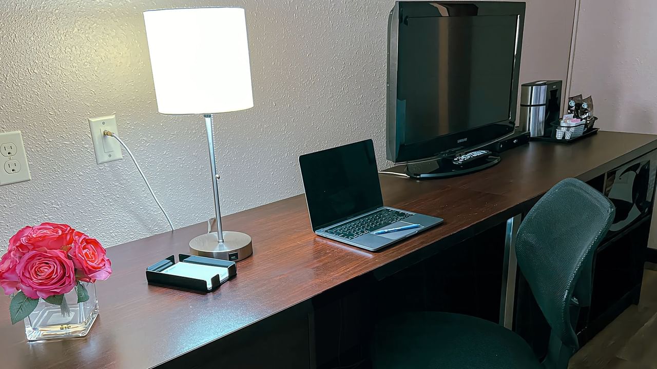 Table with computer, lamp, TV, coffee and tea, and flowers