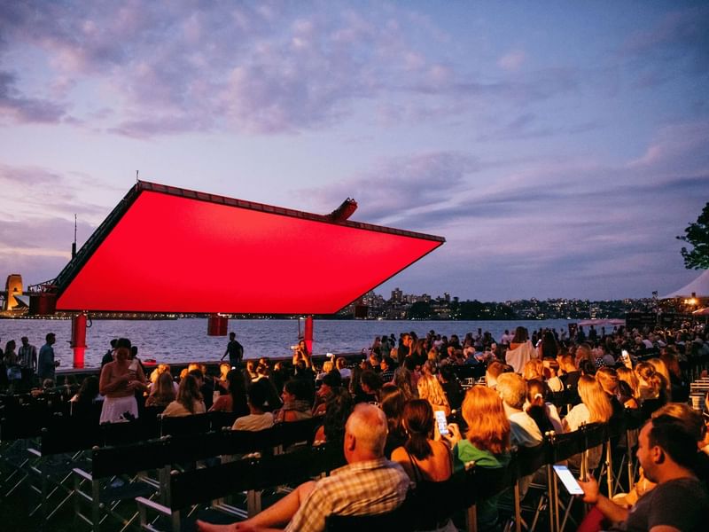 Crowd watching a film under a red screen at Westpac OpenAir Cinema.