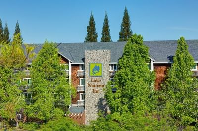 Front view of Lake Natoma Inn with a prominent stone sign, surrounded by lush green trees