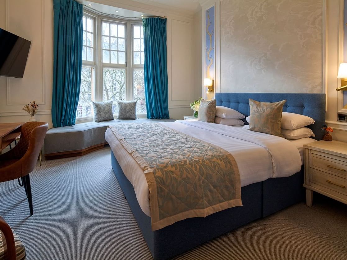 Club room with blue upholstered bed, bay window seating, and elegant décor at Sloane Square Hotel with window view overlooking Sloane Square or Holy Trinity Church 