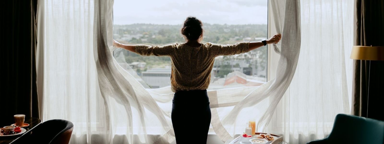 Woman with arms outstretched standing in front of a window with white curtains.