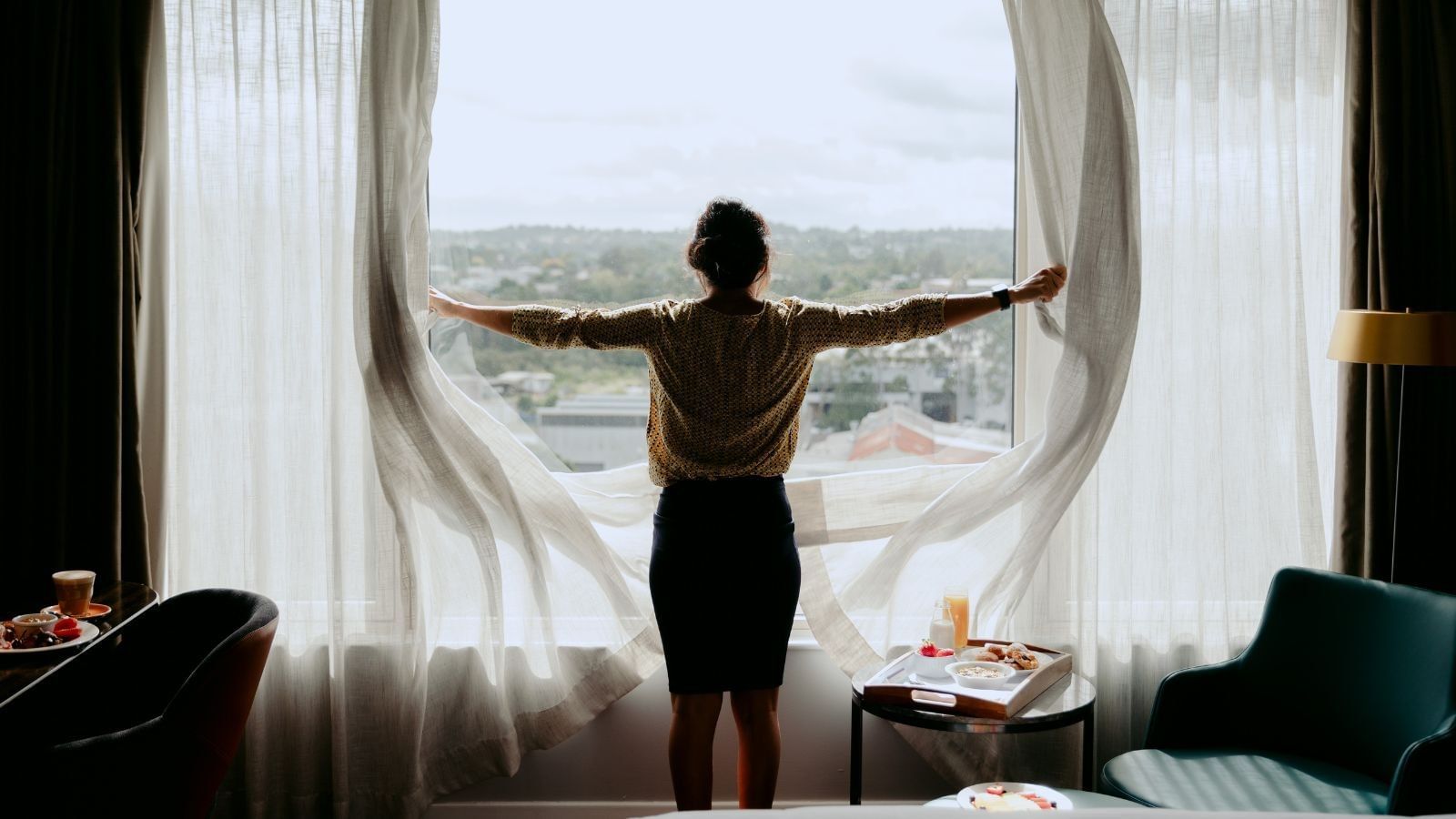 Woman with arms outstretched standing in front of a window with white curtains.