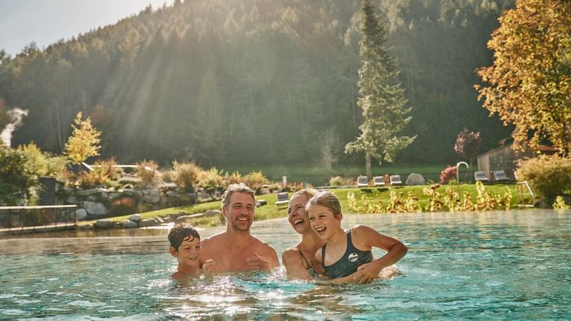 Famiglia felice in piscina all'aperto con sfondo di alberi e colline.