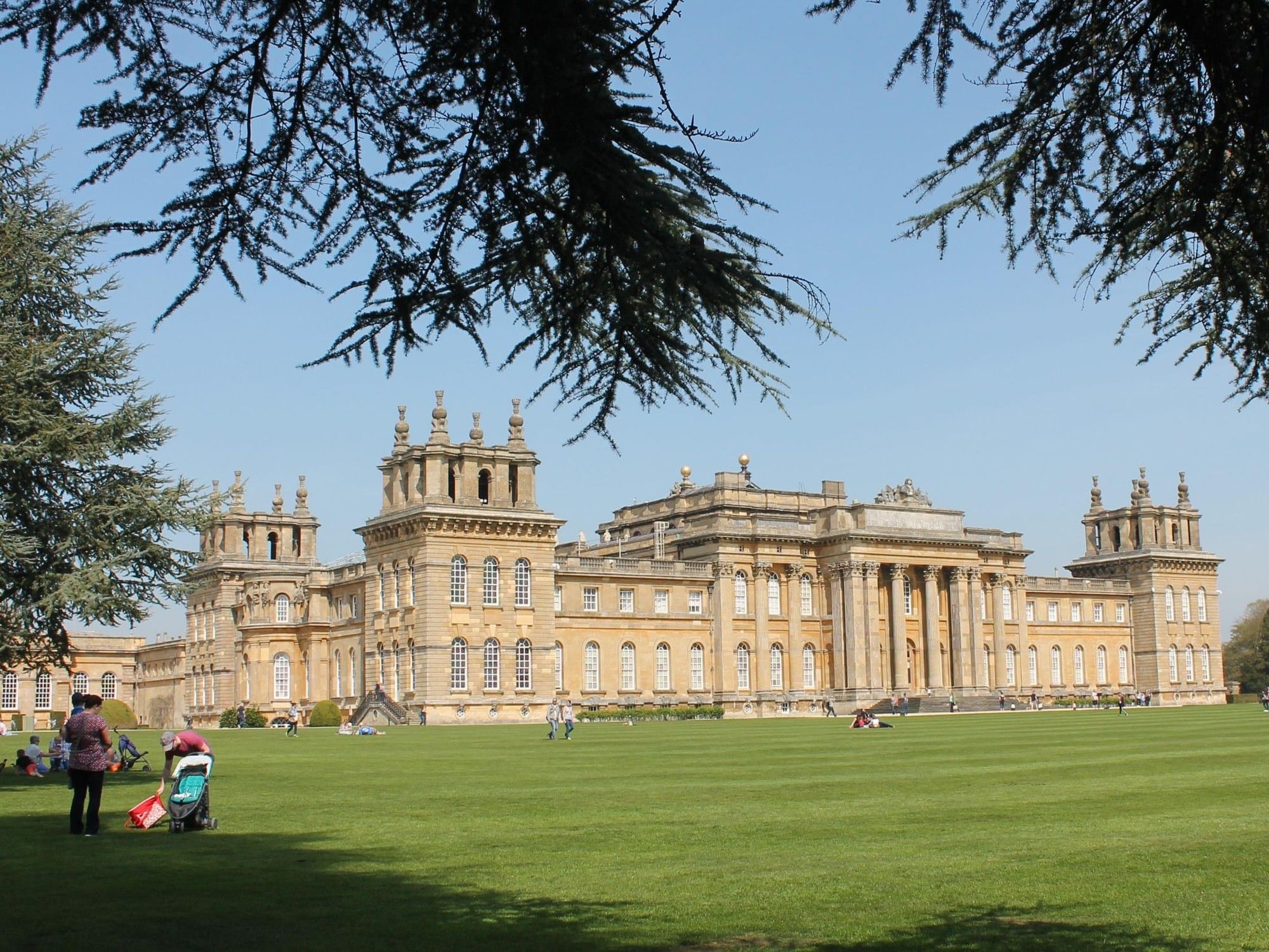 Blenheim Palace with ornate towers and columns set in expansive green grounds under a clear blue sky.