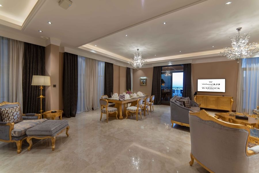 Gilded dining set by plush velvet armchairs under ornate crystal chandeliers in Penthouse Villa at Warwick Al Khobar