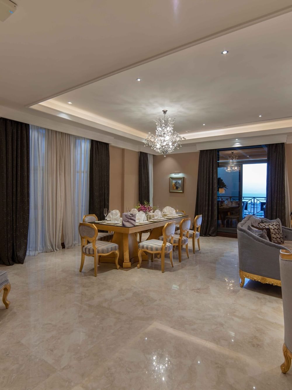 Gilded dining set by plush velvet armchairs under ornate crystal chandeliers in Penthouse Villa at Warwick Al Khobar