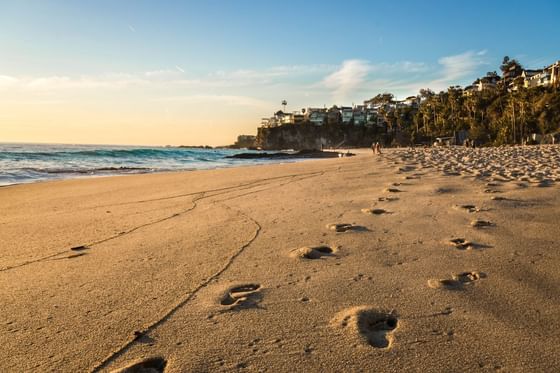 Footprints on a sandy beach by the ocean under a sunset glow near Anaheim Portofino Inn & Suites