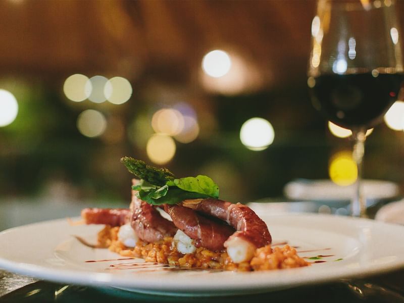 Gourmet dish with prosciutto-wrapped meat and a glass of red wine, served at Fiesta Americana