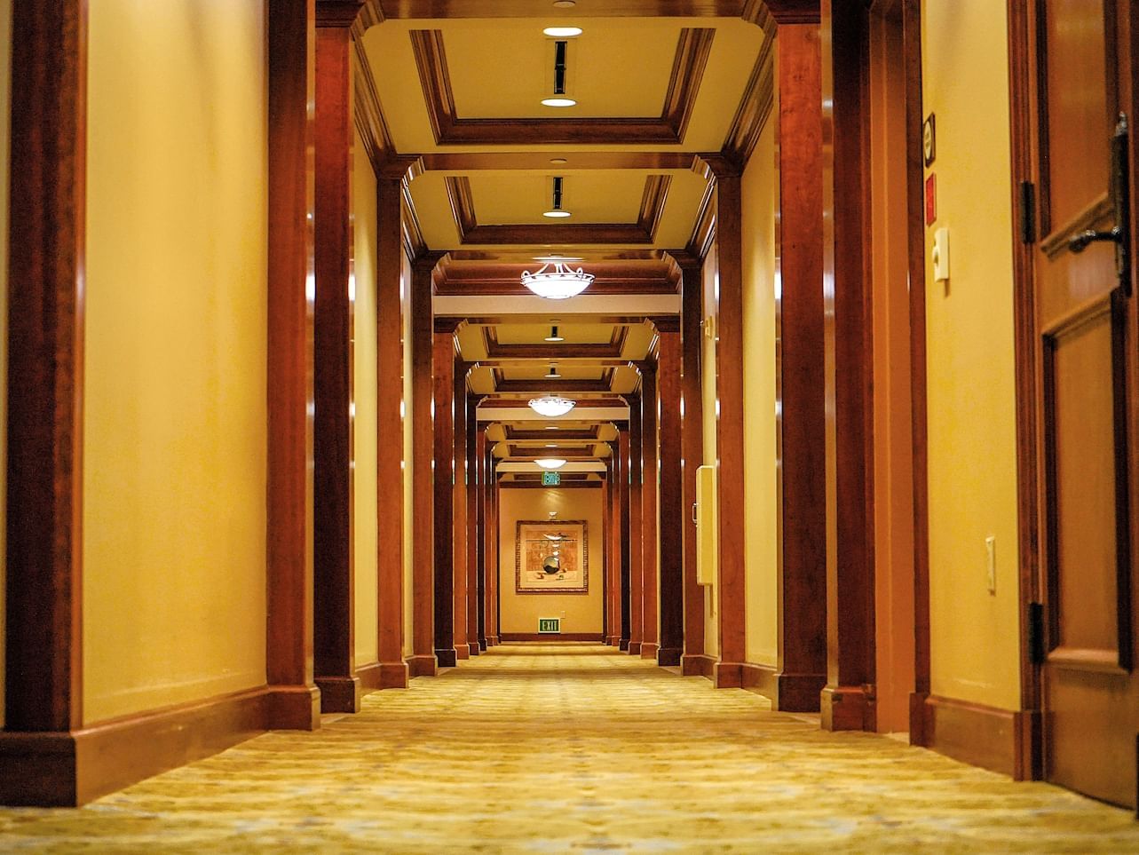 Well-lit hotel hallway featuring wood-paneled walls, plush carpet, and decorative lighting at The Rose Hotel