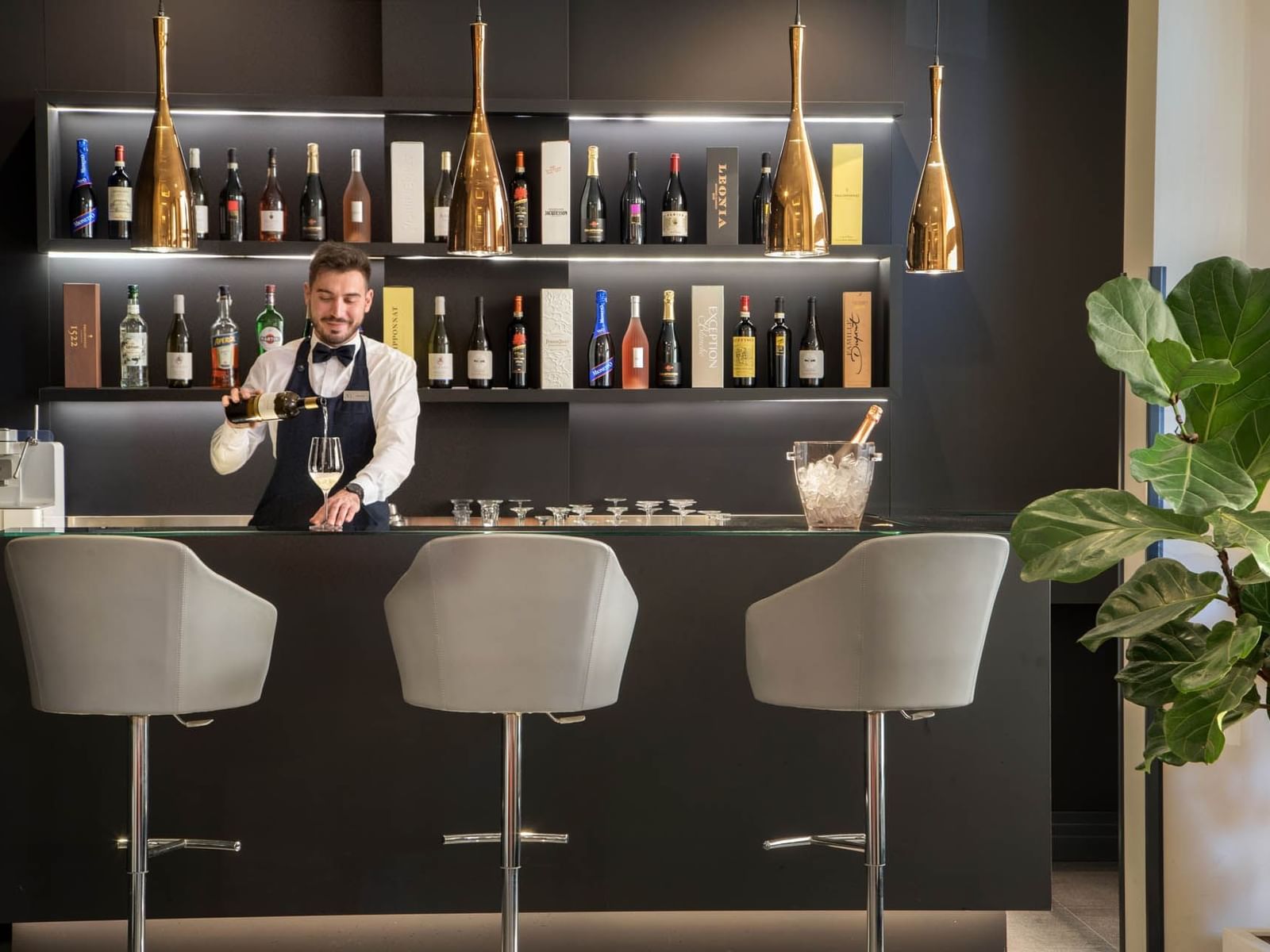 A bartender in a bow tie pours a drink at a bar, surrounded by colorful bottles and elegant lighting at The Republic Hotel