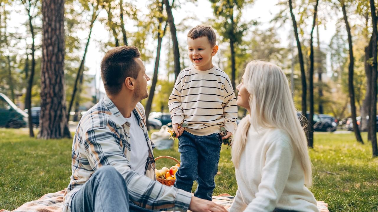 A family with a young boy is sitting on a blanket in a park.