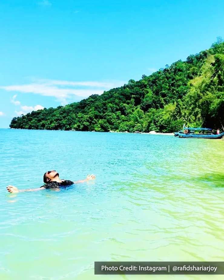 A person floats in shallow water near a beach - Lexis Suites Penang