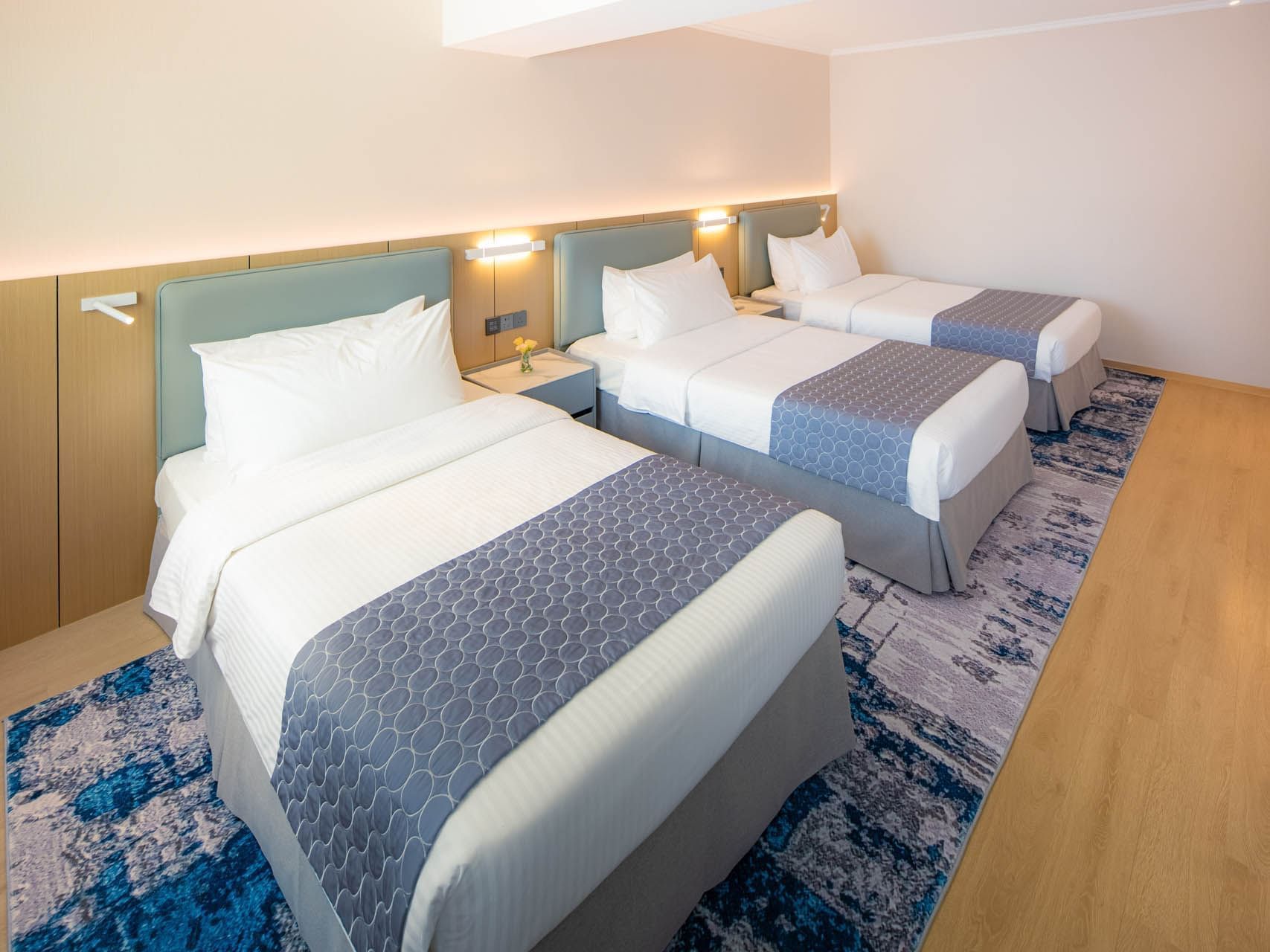 Deluxe Triple Room with three single beds, blue patterned bed runners, and a colorful area rug at Inn Hotel Macau