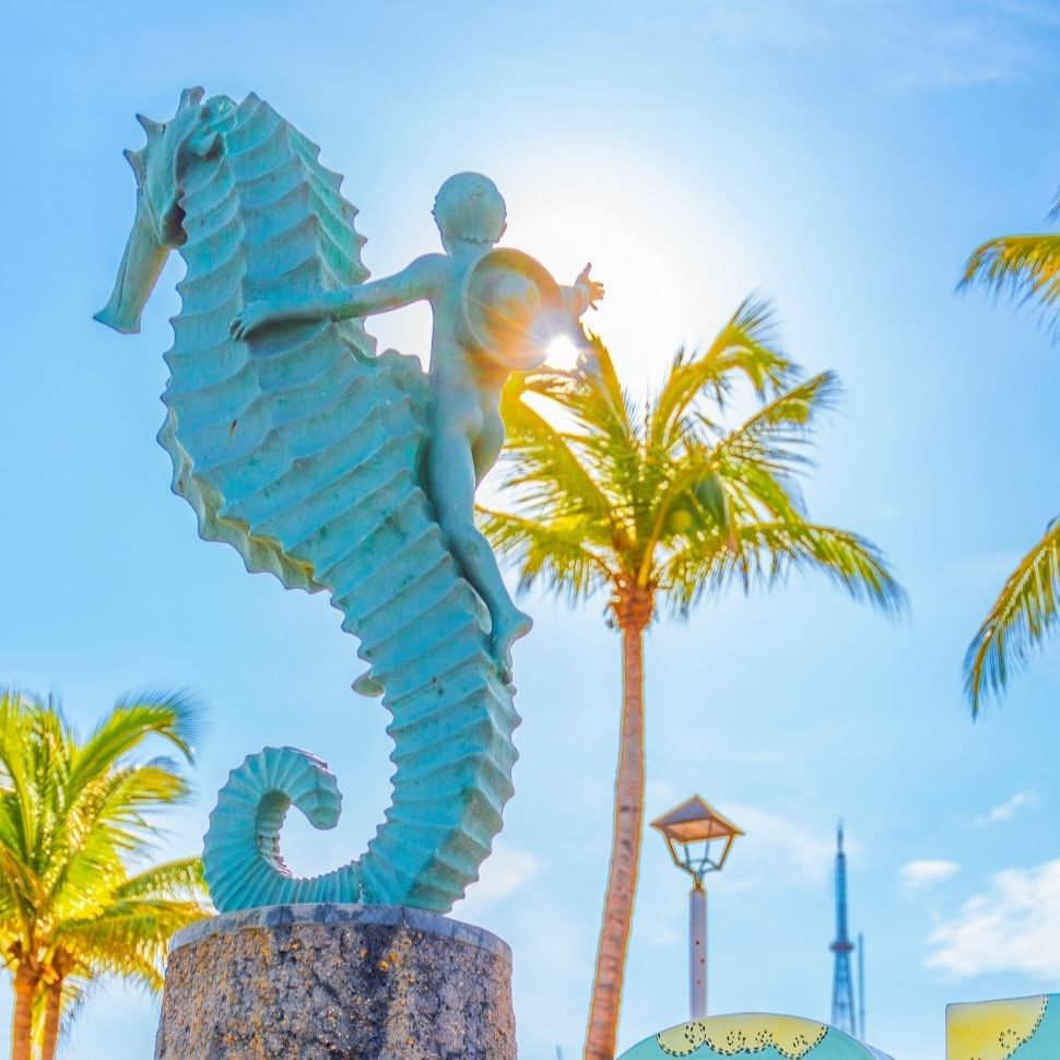 Escultura de un niño cabalgando un caballito de mar en Puerto Vallarta, rodeada de letras decoradas y palmeras.