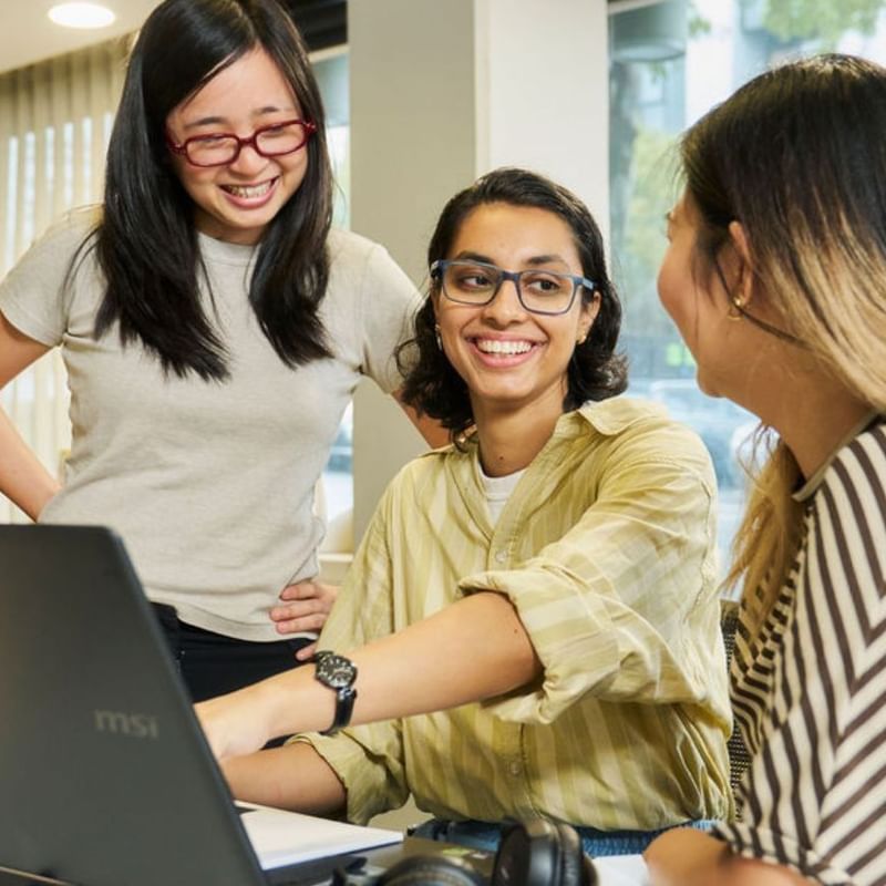 Three residents smiling and working together on a laptop at Student Living on Villiers.