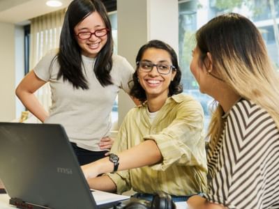 Three residents smiling and working together on a laptop at Student Living on Villiers.