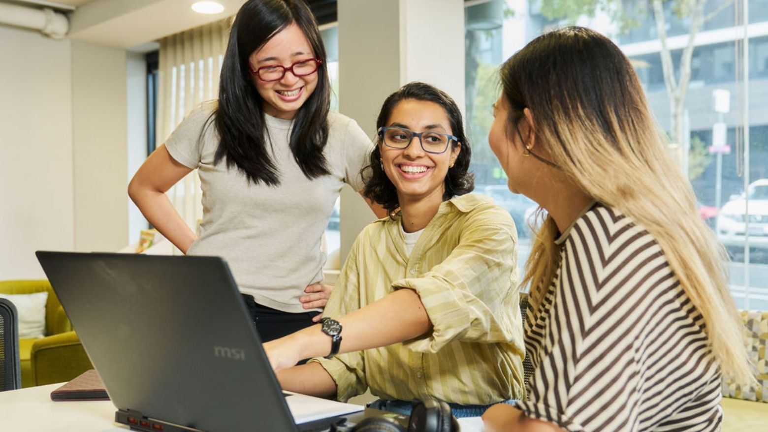 Three residents smiling and working together on a laptop at Student Living on Villiers.