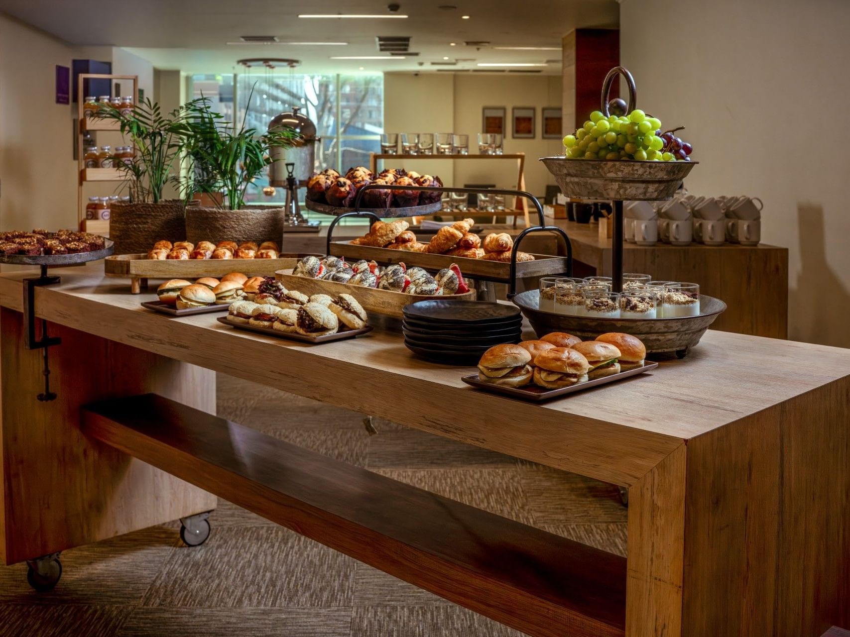 Mesa de bufé de madera con una variedad de pasteles, fruta y bebidas en un hotel.