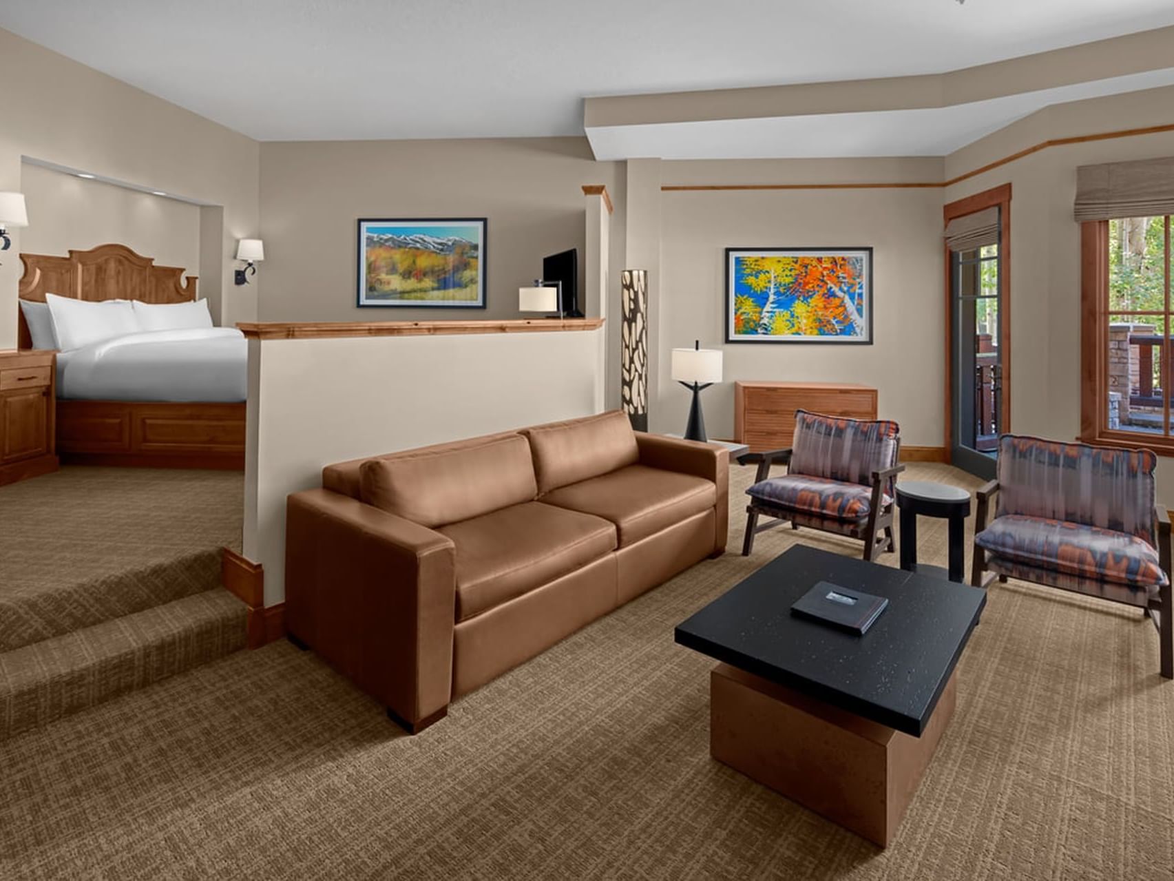 Living area with sofa, table, cozy bed & wall art in Deluxe Executive Suite at Hotel Park City Autograph Collection