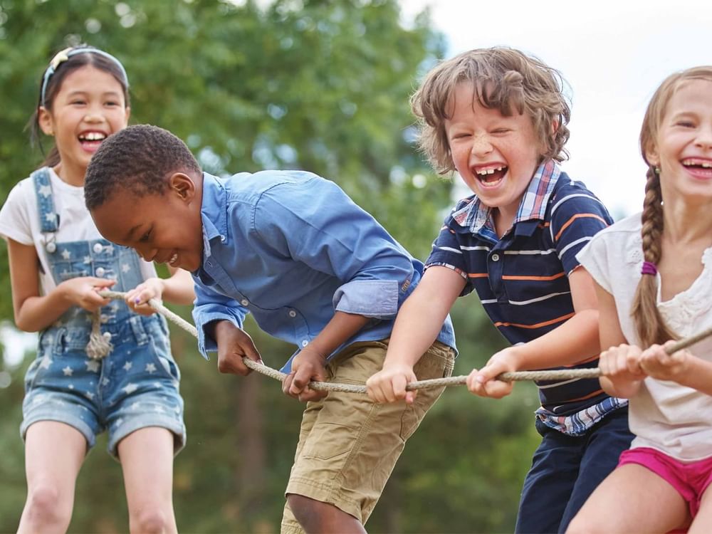 Children laughing and playing tug of war in a park for the Easter guide.