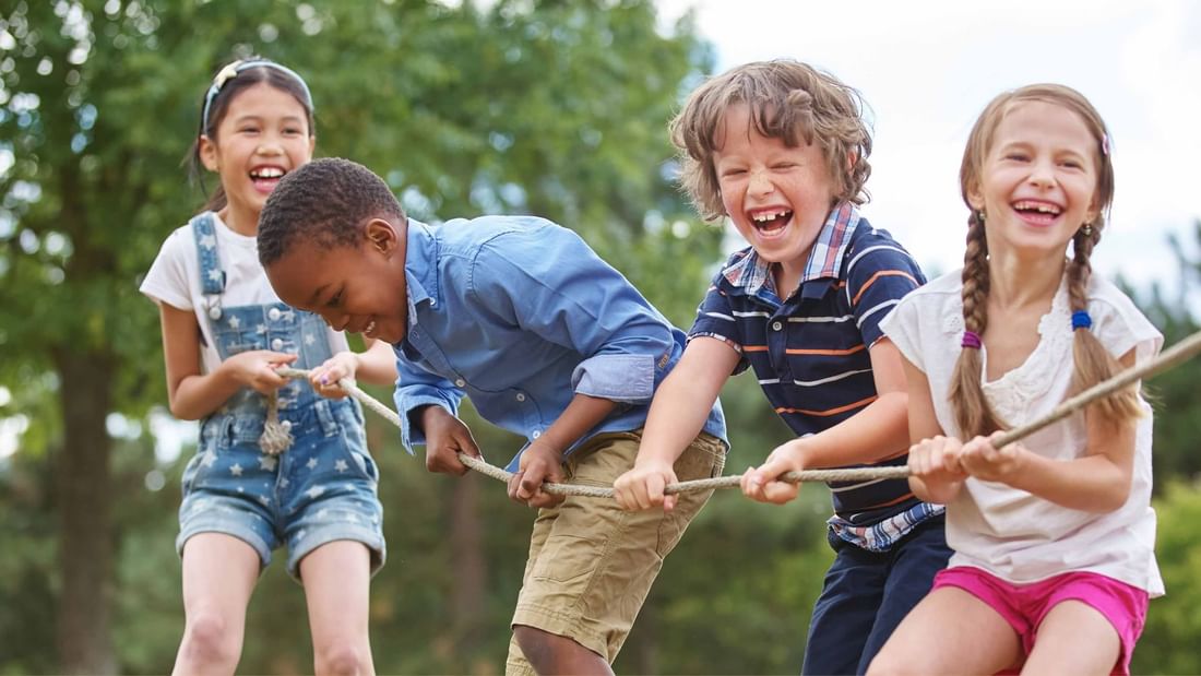 Children laughing and playing tug of war in a park for the Easter guide.