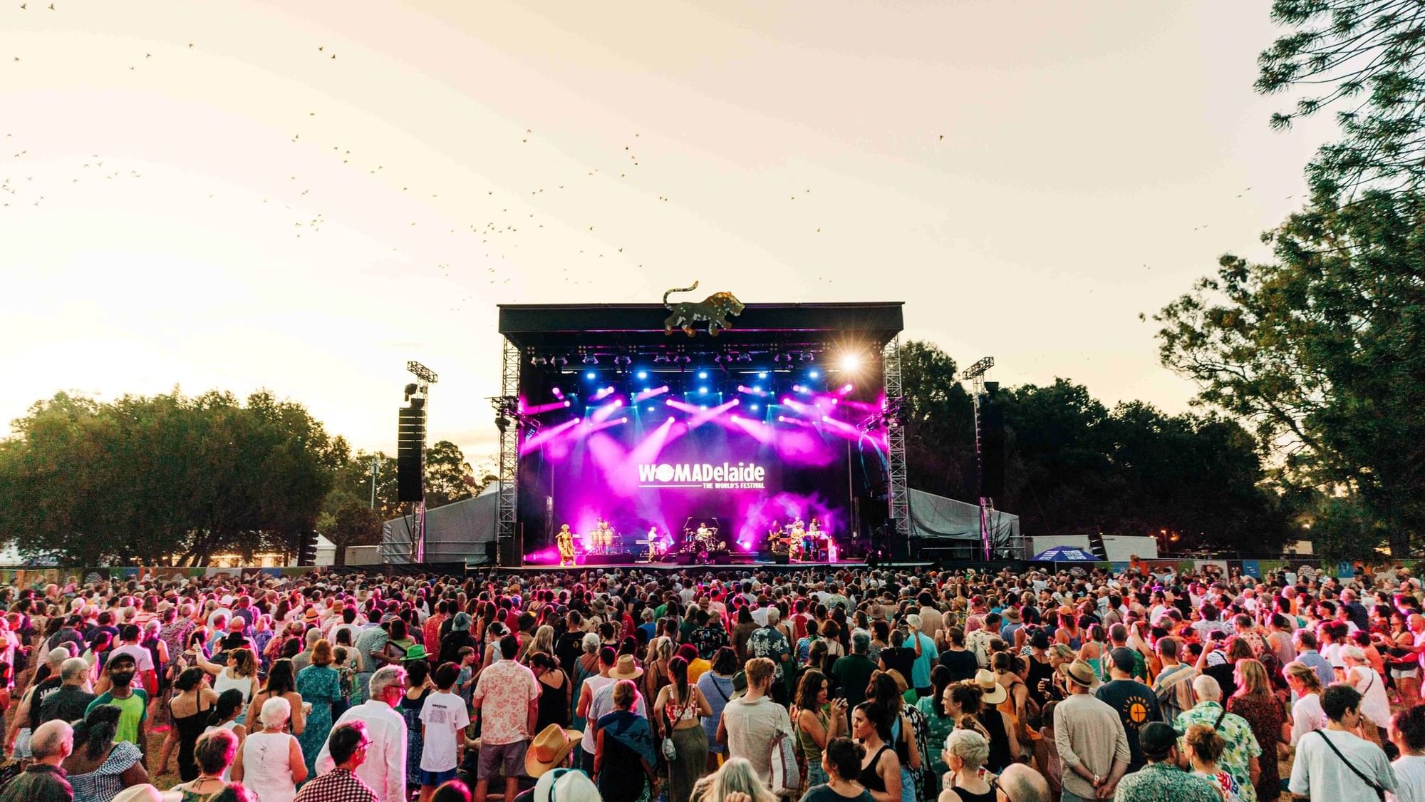 Large crowd at WOMADelaide festival with performers on stage under colorful lights.