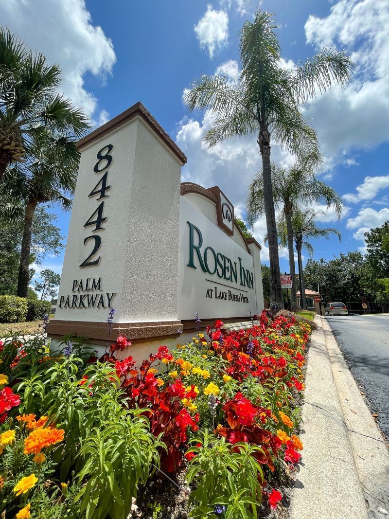 The Rosen Inn at Lake Buena Vista sign, with its address (8442 Palm Parkway) displayed in dark letters on a light background among colorful flowerbeds and palm trees. An advantage of staying at the Rosen Inn at Lake Buena Vista is the peace of mind provided by 24/7 security. 